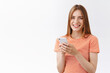 © Cookie Studio - Friendly, pretty young carefree woman in striped t-shirt hold smartphone, smiling and gazing camera delighted, browsing internet, making phone call, texting funny story, stand white background