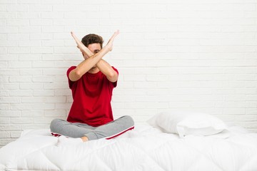 Wall Mural - Young teenager student man on the bed keeping two arms crossed, denial concept.