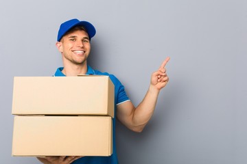 Wall Mural - Young man delivering packages smiling cheerfully pointing with forefinger away.