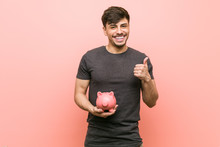 Young Hispanic Man Holding Piggy Bank Smiling And Raising Thumb Up