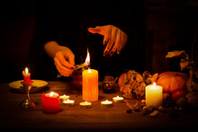 Witch Burns A Herb On The Altar In The Dark. Female Hands With Sharp Black Nails Do Magic Among Candles, Pumpkin, Nuts, Dry Leaves, Selected Focus, Low Key