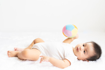 A cute 6 months old asian little baby boy is playing and carrying the ball with happiness moment on the bed in the morning time, concept of healthy and child development in the first year of life.