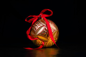 Shiny red and gold geometric Christmas bauble/ bulb with a red ribbon tied into a bow on top, and isolated onto a black background. 