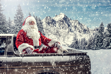 Wall Mural - Bearded in red clothes sits on the back of a white truck.Santa distributes gifts for children.Landscape of mountains and winter forest covered with snow and frost.Christmas time.Copy space.Snowflakes 