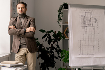 Poster - Serious architect or engineer with his arms crossed on chest standing by window