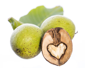 heart shaped halfed walnut kernel in front of 2 fresh green walnuts on a branch with an leaf isolated on white background