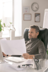 Poster - Mature confident architect looking at sketches on papers while sitting by desk