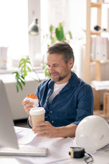 Poster - Happy mature engineer looking at funny cupcake in his hand before eating it