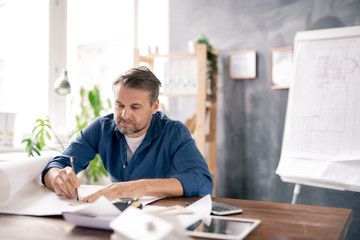 Poster - Mature architect in casualwear drawing line on blueprint while making sketch