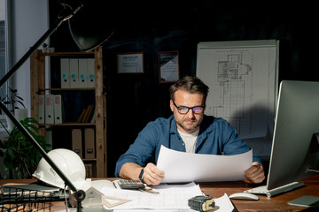 Poster - Mature architect looking at sketch while working in office late in the evening