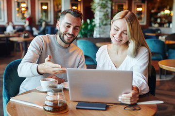 Smiling guy making presentation to his pretty girlfriend or groupmate in cafe