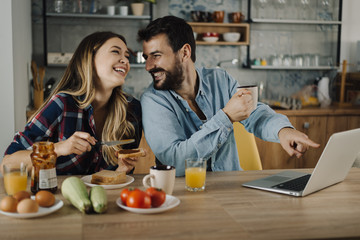 Wall Mural - Young happy couple enjoying in breakfast time and surfing the net on laptop