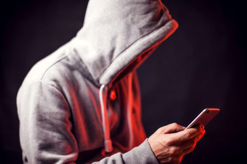 Man wearing hoody sweater with phone in hands. Crime and hacking concept