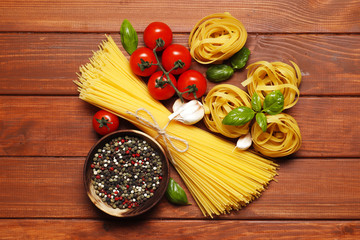 Uncooked fettuccine ball, different pasta, ingredients for sauce. cherry tomatoes, , spices, oil, basil on a wooden background. top view. Place for text.