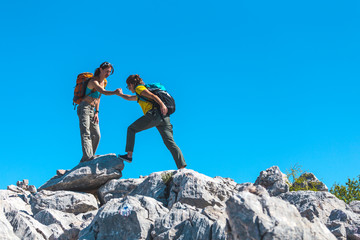 A woman helps her friend climb a stone.