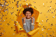 © WHstudio Leushin N - Image of optimistic dark skinned lady clenches fists joyfully, celebrates victory, dressed in striped clothing, has eyes shut, poses in paper hole against yellow background. Triumphing and win concept