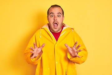 Sticker - Young man wearing rain coat standing over isolated yellow background celebrating crazy and amazed for success with arms raised and open eyes screaming excited. Winner concept