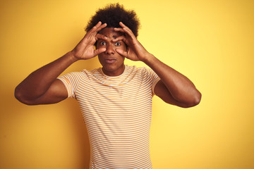 Sticker - American man with afro hair wearing striped t-shirt standing over isolated yellow background Trying to open eyes with fingers, sleepy and tired for morning fatigue