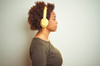 © Krakenimages.com - African american woman wearing headphones listening to music over isolated background looking to side, relax profile pose with natural face with confident smile.