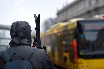 Man is going to go skiing. Boy in a hood with a backpack behind his back holds skis in his hands and is going to carry hand luggage by public transport. Man with skis waiting for a bus. Winter sports