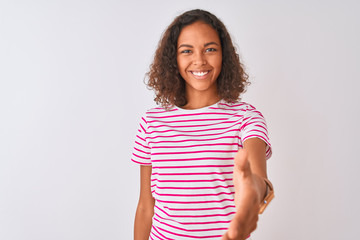 Wall Mural - Young brazilian woman wearing pink striped t-shirt standing over isolated white background smiling friendly offering handshake as greeting and welcoming. Successful business.