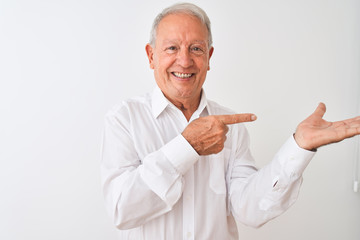 Poster - Senior grey-haired man wearing elegant shirt standing over isolated white background amazed and smiling to the camera while presenting with hand and pointing with finger.