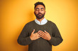 © Krakenimages.com - Young indian man wearing green sweater and shirt standing over isolated yellow background smiling with hands on chest with closed eyes and grateful gesture on face. Health concept.