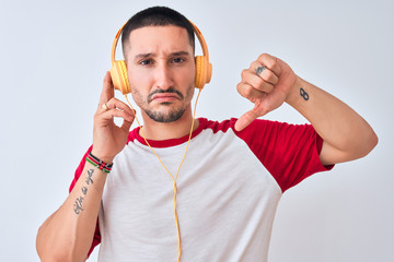 Poster - Young handsome man wearing headphones over isolated background with angry face, negative sign showing dislike with thumbs down, rejection concept