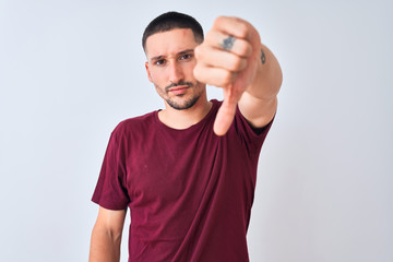 Sticker - Young handsome man standing over isolated background looking unhappy and angry showing rejection and negative with thumbs down gesture. Bad expression.