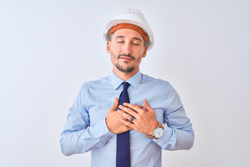 Sticker - Young business man wearing contractor safety helmet over isolated background smiling with hands on chest with closed eyes and grateful gesture on face. Health concept.