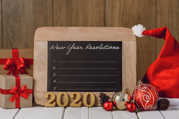 Wall Mural - 2020 wooden text and Christmas ornaments and New Year's Resolutions List written on chalkboard over wooden background