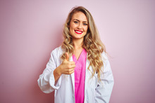 Young Beautiful Doctor Woman Standing Over Pink Isolated Background Doing Happy Thumbs Up Gesture With Hand. Approving Expression Looking At The Camera With Showing Success.