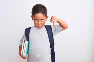 Wall Mural - Beautiful student kid boy wearing backpack holding books over isolated white background with angry face, negative sign showing dislike with thumbs down, rejection concept