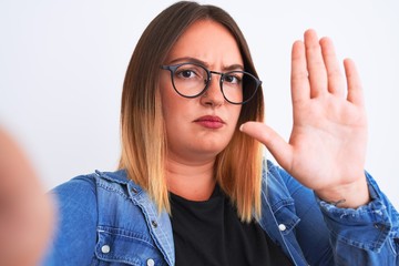 Sticker - Beautiful woman wearing denim shirt and glasses make selfie over isolated white background with open hand doing stop sign with serious and confident expression, defense gesture