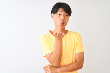 Chinese man wearing yellow casual t-shirt standing over isolated white background looking at the camera blowing a kiss with hand on air being lovely and sexy. Love expression.