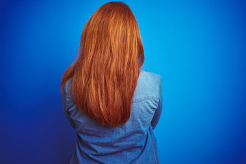 Sticker - Young beautiful redhead woman wearing denim shirt standing over blue isolated background standing backwards looking away with crossed arms