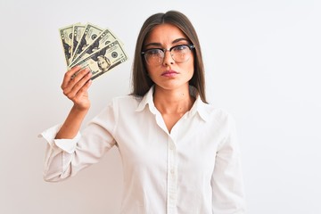 Wall Mural - Beautiful businesswoman wearing glasses holding dollars over isolated white background with a confident expression on smart face thinking serious