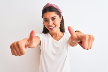 Wall Mural - Young beautiful woman wearing casual t-shirt and diadem over isolated white background approving doing positive gesture with hand, thumbs up smiling and happy for success. Winner gesture.