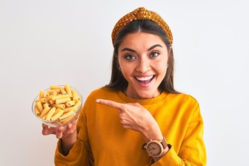 Wall Mural - Young beautiful woman holding bowl with macaroni pasta over isolated white background very happy pointing with hand and finger