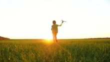 A Happy Little Boy Runs Across A Green Meadow Playing With A Toy Airplane, Imagining Flying.