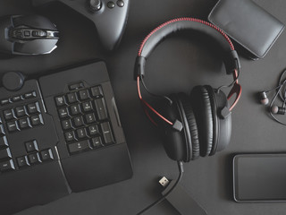 gamer work space concept, top view a gaming gear, mouse, keyboard, joystick, headset and in ear headphone on black table background.