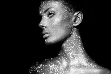 Fashion model woman in bright sparkles and lights posing in studio. Portrait of beautiful sexy woman. Art design glitter glowing make up. Black and white photography