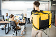 Courier delivering products for office workers, carrying yellow thermal bag, view from the back side. Concept of food delivery to employees in the office