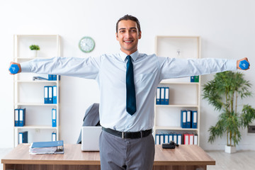 Young handsome employee doing sport exercises at workplace