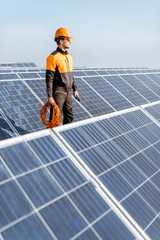 Wall Mural - Well-equipped worker in protective orange clothing servicing solar panels on a photovoltaic rooftop plant. Concept of maintenance and installation of solar stations