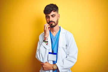 Poster - Young doctor man with tattoo wearing id card standing over isolated yellow background thinking looking tired and bored with depression problems with crossed arms.