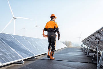 Wall Mural - Well-equipped worker in protective orange clothing walking and examining solar panels on a photovoltaic rooftop plant. Concept of maintenance and installation of solar stations