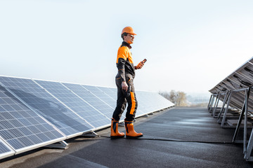 Wall Mural - well-equipped worker in protective orange clothing walking and examining solar panels on a photovolt
