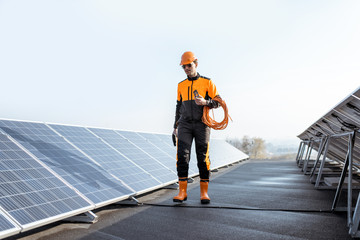 Wall Mural - Well-equipped worker in protective orange clothing walking and examining solar panels on a photovoltaic rooftop plant. Concept of maintenance and installation of solar stations