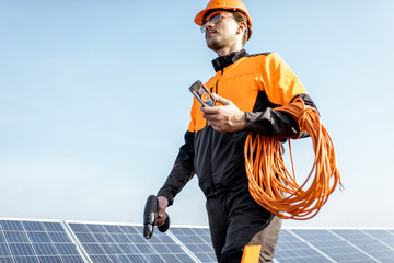 Wall Mural - well-equipped worker in protective orange clothing servicing solar panels on a photovoltaic rooftop 